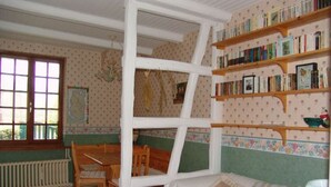 A cozy room with a white-framed window, a wooden chair, a sofa with striped cushions, and a bookshelf filled with books. - Cozy rooms in the heart of the Argonne forest (Futeau)