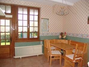 A dining area with a wooden table and chairs, a radiator below a window, and a wall with a polka dot pattern. - Cozy rooms in the heart of the Argonne forest (Futeau)