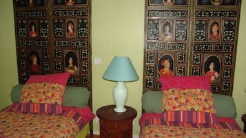 Een kamer met twee bedden, elk met een bloemenbedekking en een groen kussen. Tussen de bedden staat een houten nachtkastje met een witte lamp.