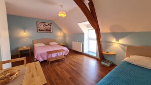 Une chambre mansardée chaleureuse avec un plafond en pente, un lit recouvert d’une couverture rose, une table en bois avec un panier, et une autre couverture bleue sur le lit.