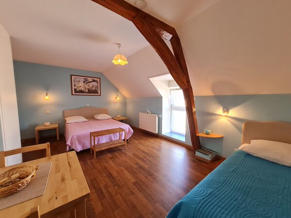 A cozy attic bedroom with a sloped ceiling, a bed with a pink bedspread, a wooden table with a basket, and a blue bedspread.