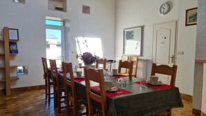 Un coin repas avec une table dressée pour six personnes, des chaises en bois, une horloge au mur et une porte avec une pancarte.