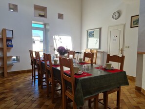 A dining area with a table set for six, wooden chairs, a clock on the wall, and a door with a sign. - Renovated farm near Beaugency, 4 rooms, homemade breakfast, near Loire à Vélo (Cravant)