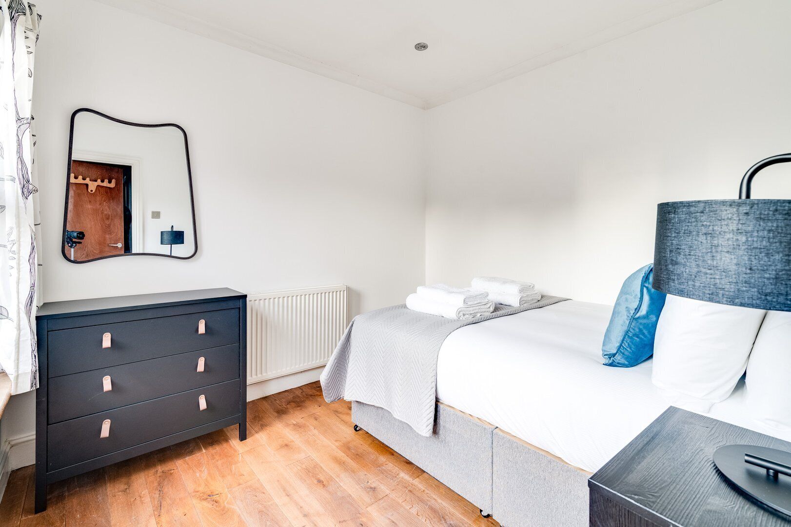 A bedroom with a bed, a dresser, a mirror, a radiator, and a lamp.