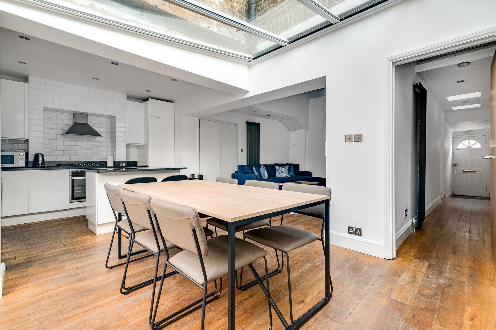 A modern kitchen with white cabinetry, a wooden dining table with four chairs, and a skylight above.