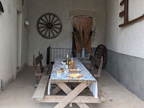 A rustic outdoor dining area with a wooden table, chairs, and a decorative wheel.