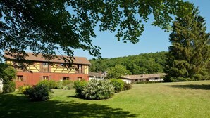 Un bâtiment traditionnel doté d’un toit en pente, entouré d’une pelouse bien entretenue et d’arbres touffus.