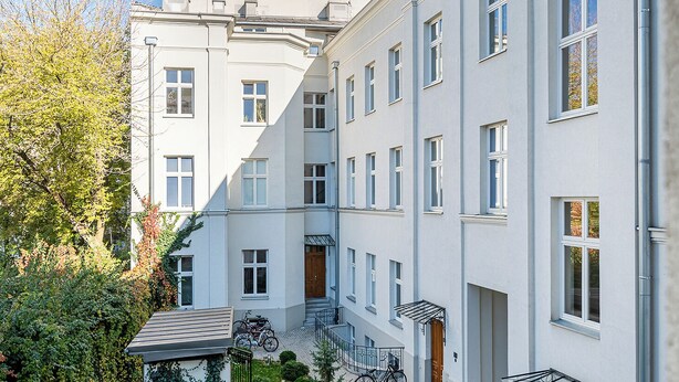 A multi-story residential building with a courtyard, a staircase, and a bike parked outside. - RentPlanet - Studio Kępna (Warsaw)