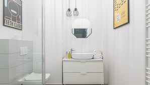 A modern bathroom with a glass shower enclosure, a white sink with a mirror above it, and a poster on the wall. - RentPlanet - Studio Kępna (Warsaw)