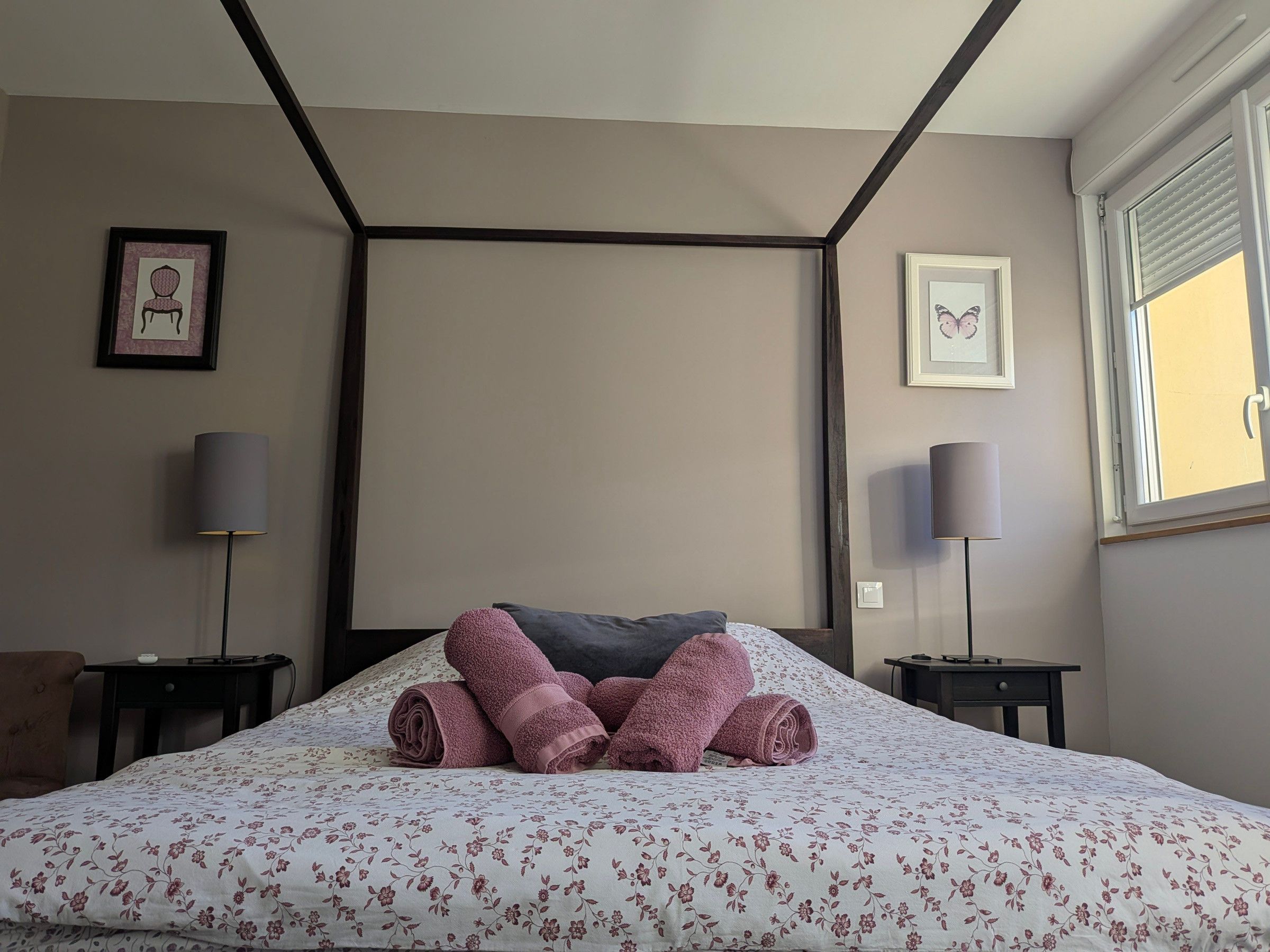 A neatly made bed with rolled towels, two bedside lamps, and framed artwork on the walls.