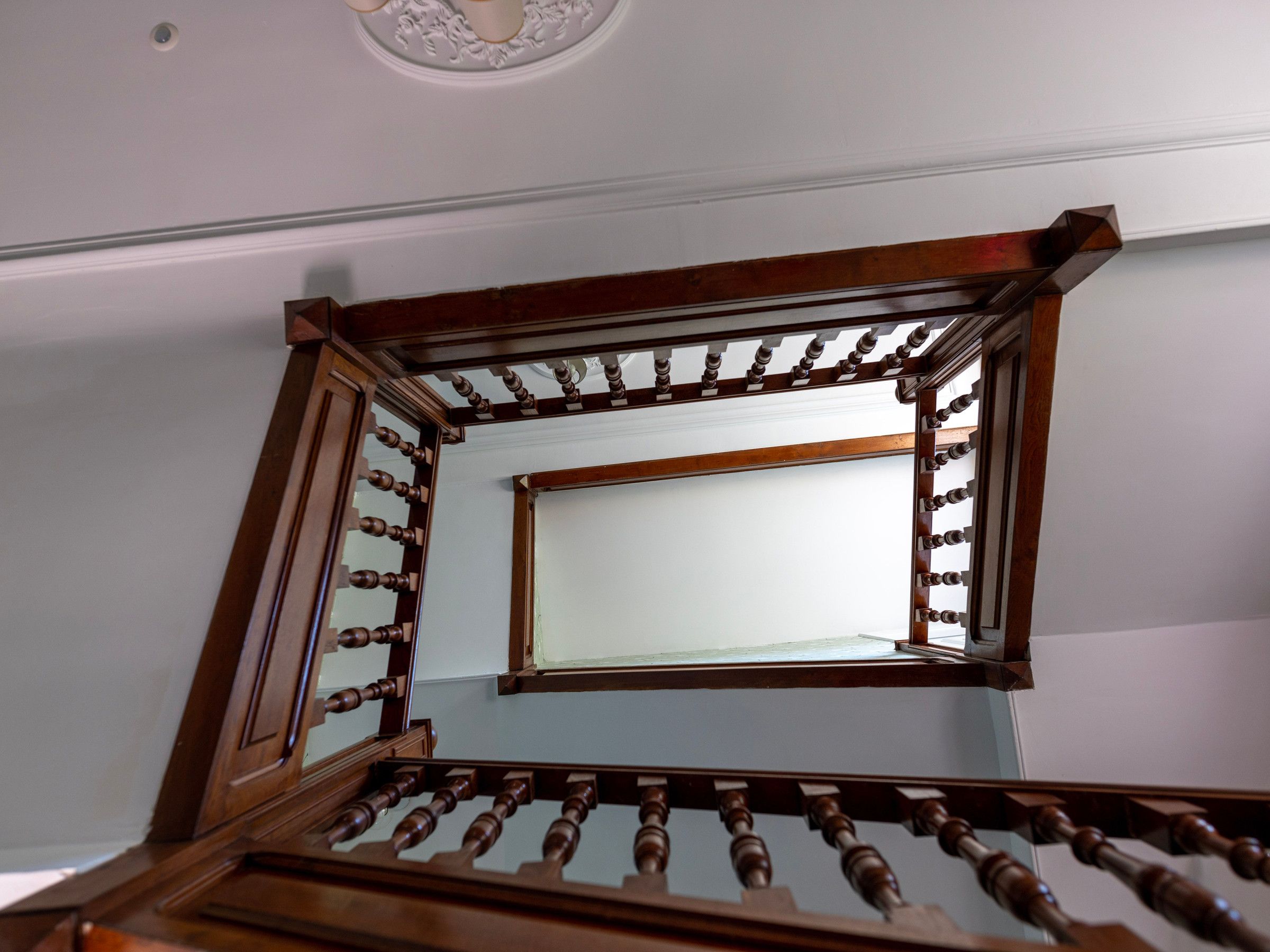 Un escalier en bois, doté d’une rampe et d’un miroir qui reflète le plafond.