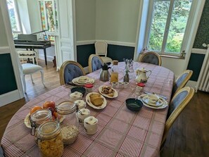 Une table à manger dressée avec différents plats, des bocaux et un piano en arrière-plan.