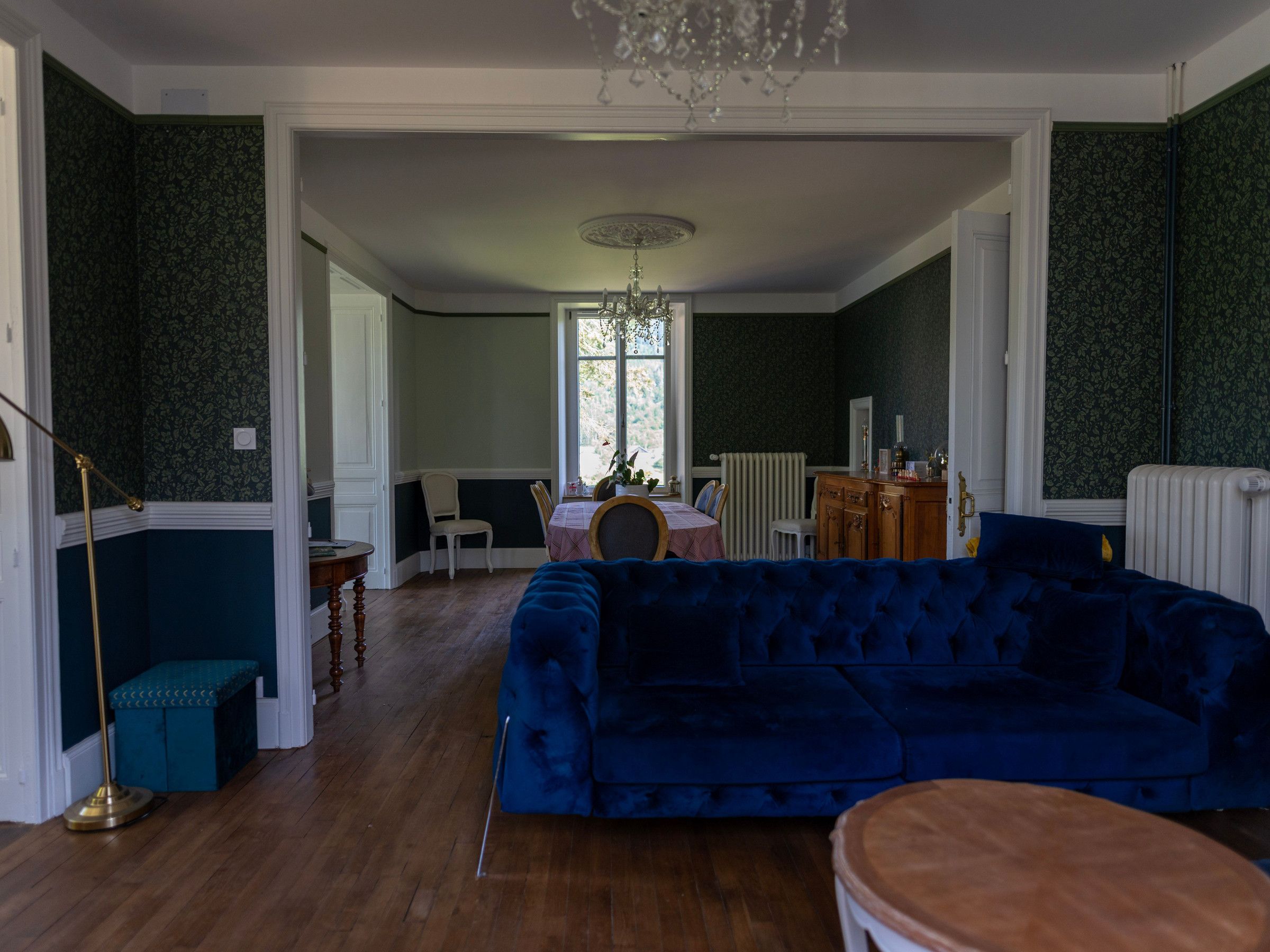 Une pièce avec un canapé bleu, un banc en bois, une table à manger avec des chaises et un lustre.