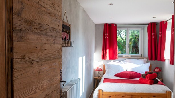 A bedroom with a wooden bed, red curtains, a window, and a radiator.