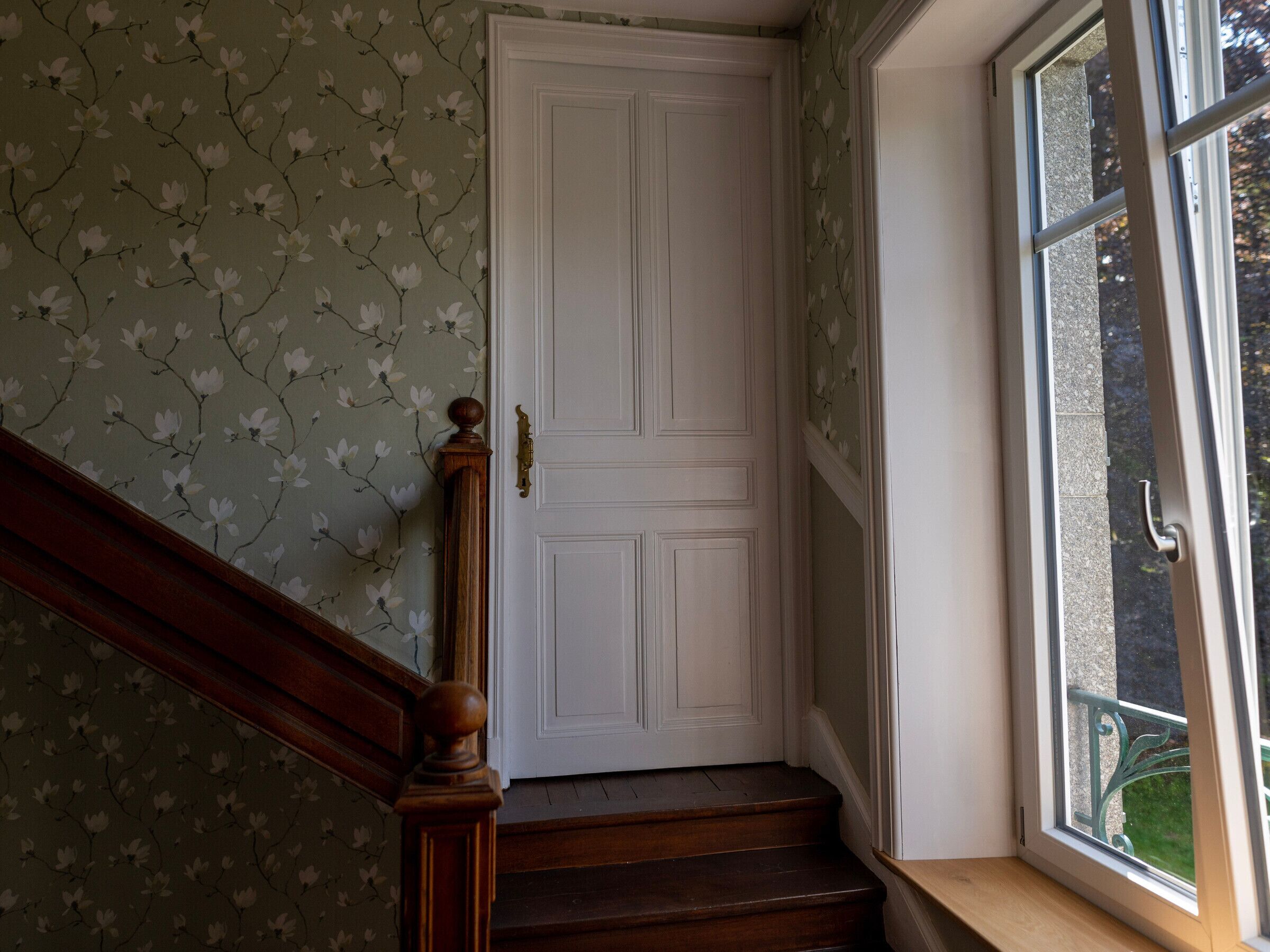 Un escalier avec une rampe en bois menant à une porte blanche dotée d’une poignée en laiton.