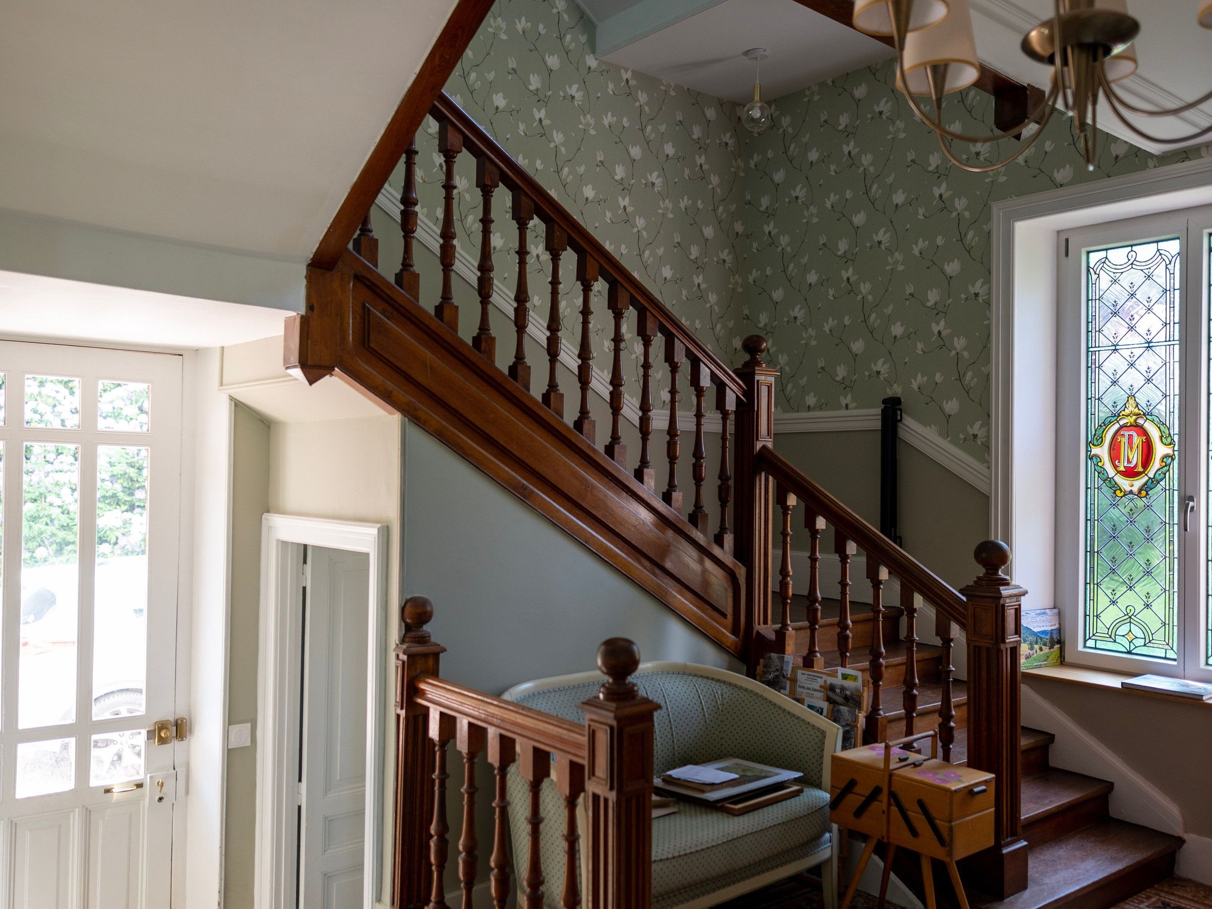 A staircase with wooden balusters, a green patterned wall, and a window with a stained glass design.