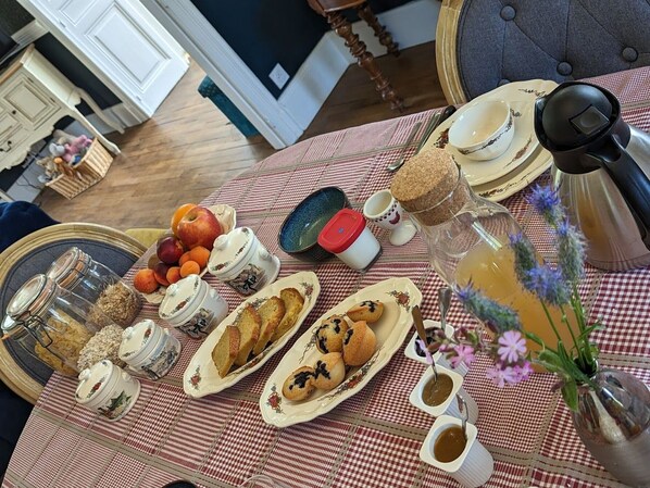 Une table de petit-déjeuner dressée avec divers aliments, notamment des fruits, des viennoiseries et des condiments, sur une nappe à carreaux.