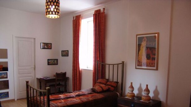 Un dormitorio con cama, escritorio, silla, armario y ventana con cortinas.
