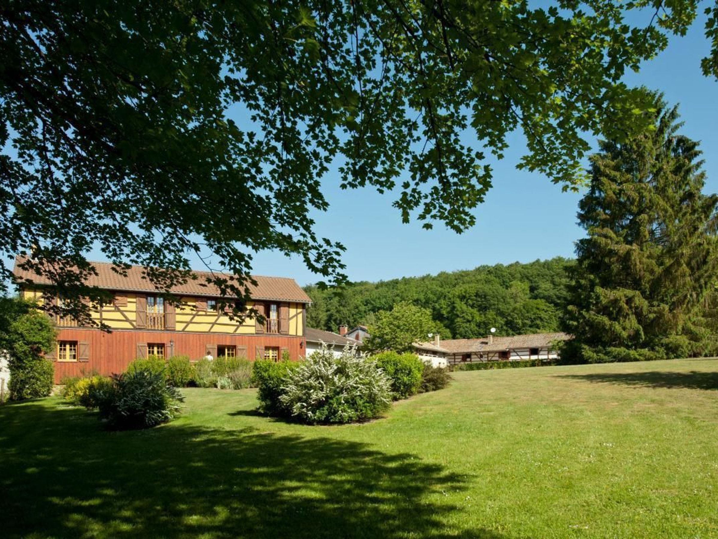 A traditional building with a sloped roof, surrounded by a well-maintained lawn and dense trees.