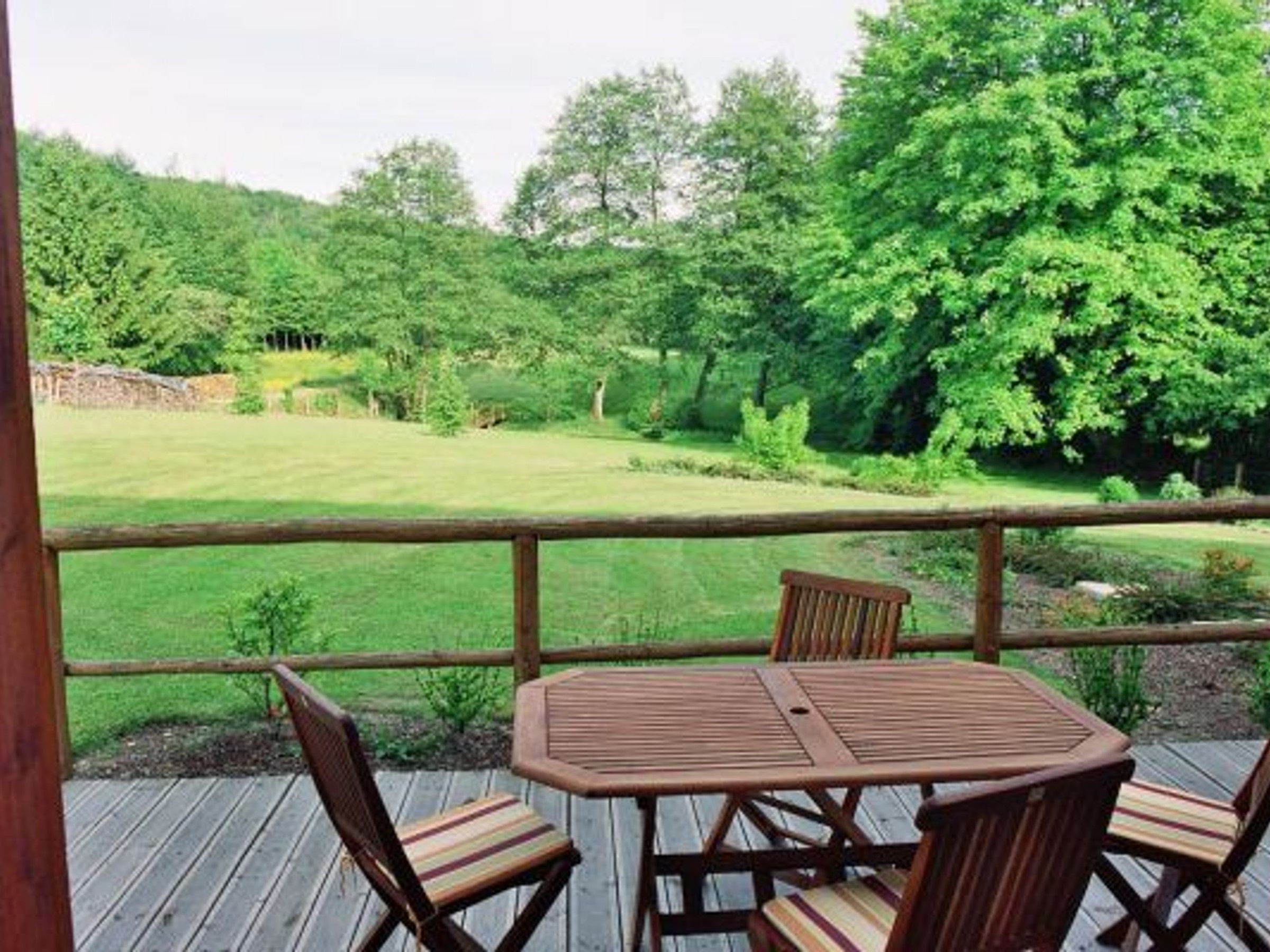Een houten terras met een tafel en stoelen, met uitzicht op een gazon met bomen.