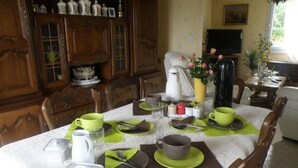 Una mesa de comedor dispuesta con platos, tazas y cubiertos verdes y marrones, rodeada de sillas de madera y un aparador con puertas de cristal.