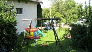 Un patio trasero con un columpio, una estructura de juego colorida y un césped.