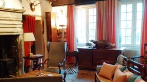 A cozy living room with a fireplace, a wooden chair, a sofa, and a table with a lamp.
