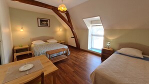 A cozy attic bedroom with a sloped ceiling, a wooden bench, a small table, a bed with a patterned bedspread, and a window providing natural light. - Spacious rooms near Beaugency, breakfast included (Cravant)