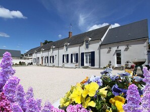 A row of white buildings with dark shutters, a gravel courtyard, and a variety of flowers in the foreground. - Spacious rooms near Beaugency, breakfast included (Cravant)