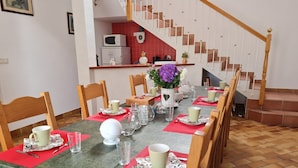 A dining area with a long table set for a meal, wooden chairs, a staircase, and a kitchen in the background. - Spacious rooms near Beaugency, breakfast included (Cravant)