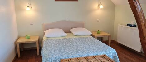 A bedroom with a bed, two bedside tables, a nightstand, a wooden bench, a framed picture on the wall, and a radiator.