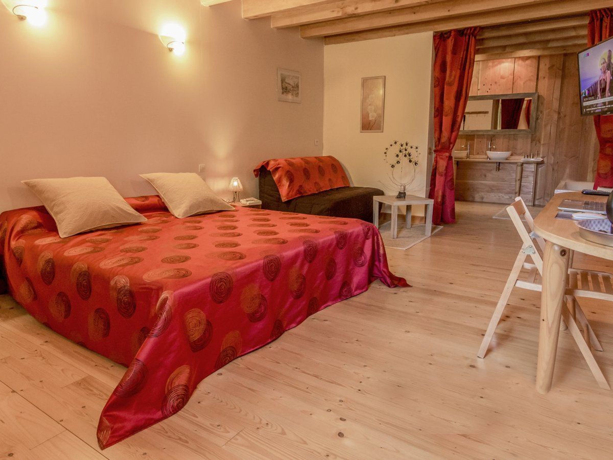A cozy bedroom with a bed, bedside table, and a small desk with a chair.