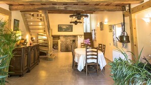 Un interior rústico con una escalera de madera, una zona de comedor con mesa y sillas, y una chimenea de piedra.