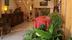Una habitación acogedora con una escalera de madera, una mesa de comedor con mantel rojo y varias plantas.