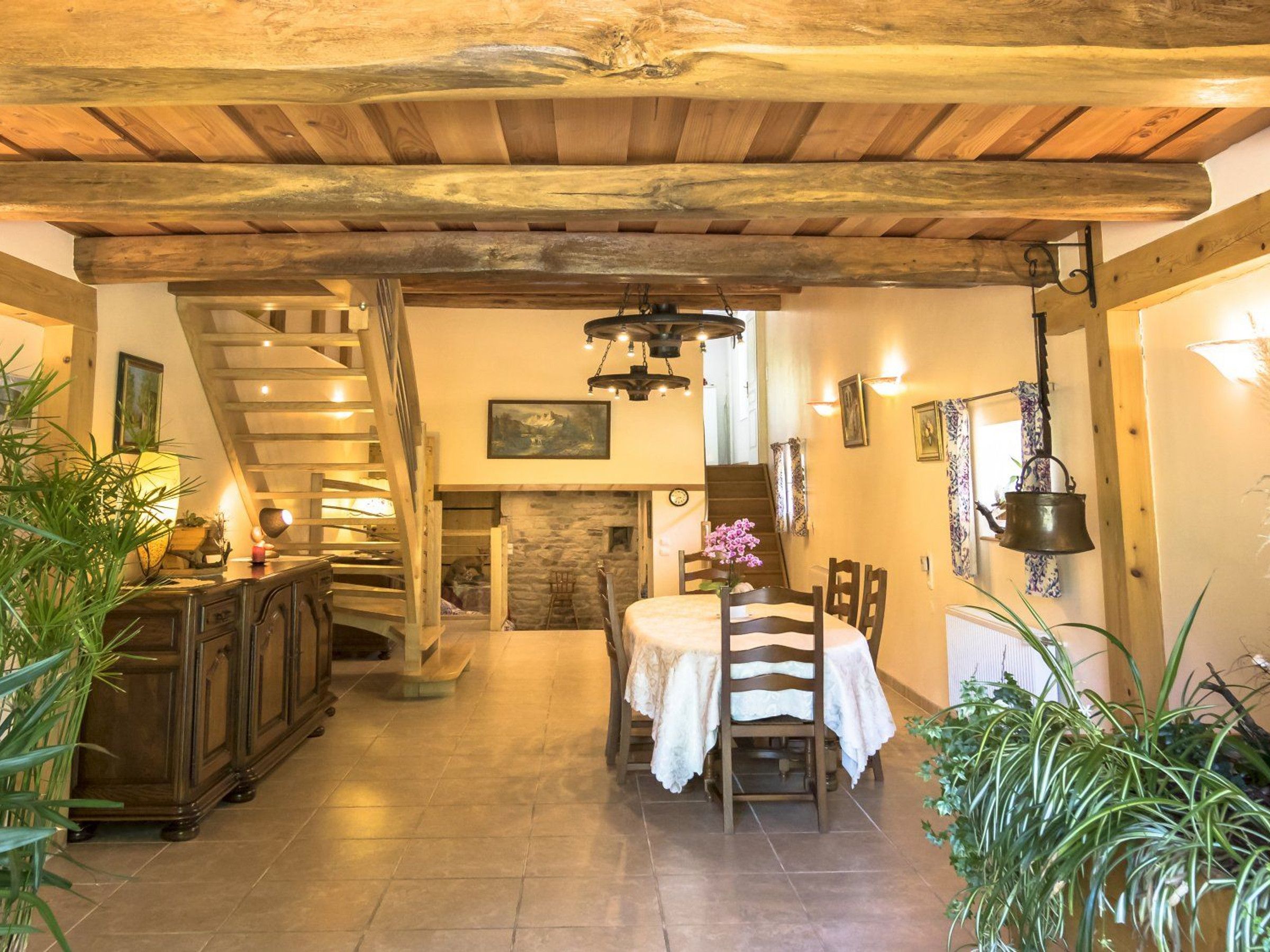 A rustic interior with a wooden staircase, a dining area with a table and chairs, and a stone fireplace.