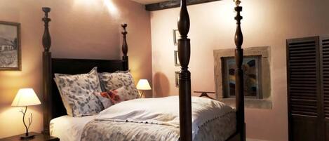 Una cama con dosel, un cabecero de madera, una mesita de noche con una lámpara y un cuadro en la pared.