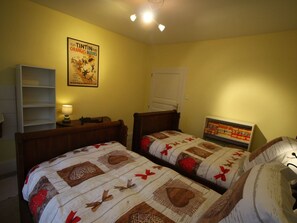 Une chambre avec deux lits simples, une table de chevet, une lampe, une affiche au mur et une fenêtre avec un store fermé.
