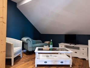Une pièce avec une table basse blanche, un fauteuil bleu et un téléviseur.