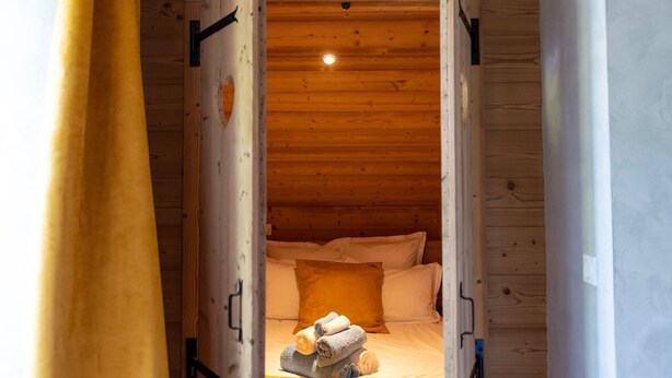 Ein gemütliches Holzblockhaus-Zimmer mit einem Bett, Kissen und einem kleinen Teppich.