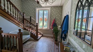 Ein Zimmer mit einer Holztreppe, einem gemusterten Teppich, einer Zimmerpflanze und einem Fenster mit dekorierter Scheibe.