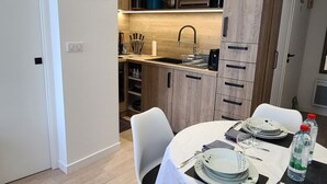 Une cuisine compacte dotée de meubles en bois, d’un évier et d’un coin repas aménagé pour deux personnes, avec assiettes et couverts.
