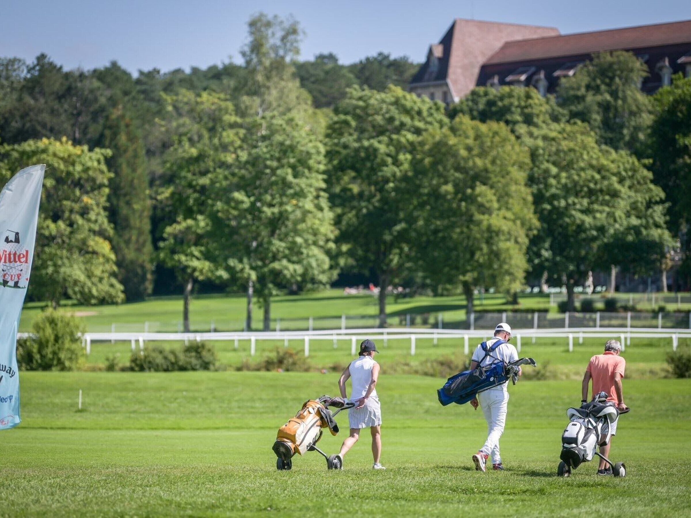 Ein Golfplatz mit Spielern, die Golftaschen tragen, und einer Fahne mit dem Text 'Wittel Cup'.