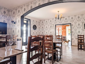 A dining area with wooden chairs and tables, a clock on the wall, and a chandelier.