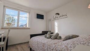 Un dormitorio con cama, escritorio, silla, ventana y televisor instalado en la pared.