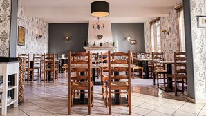 Un área de comedor con sillas y mesas de madera, una araña y papel tapiz estampado.