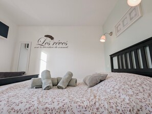 A bedroom with a bed, pillows, and a wall with a decorative phrase.