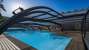 A swimming pool with a wooden deck and a covered area with a metal frame. - Spacious room with pool, spa, and hammam (Anould)