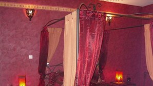A room with a four-poster bed, red walls, and two wall-mounted lamps.