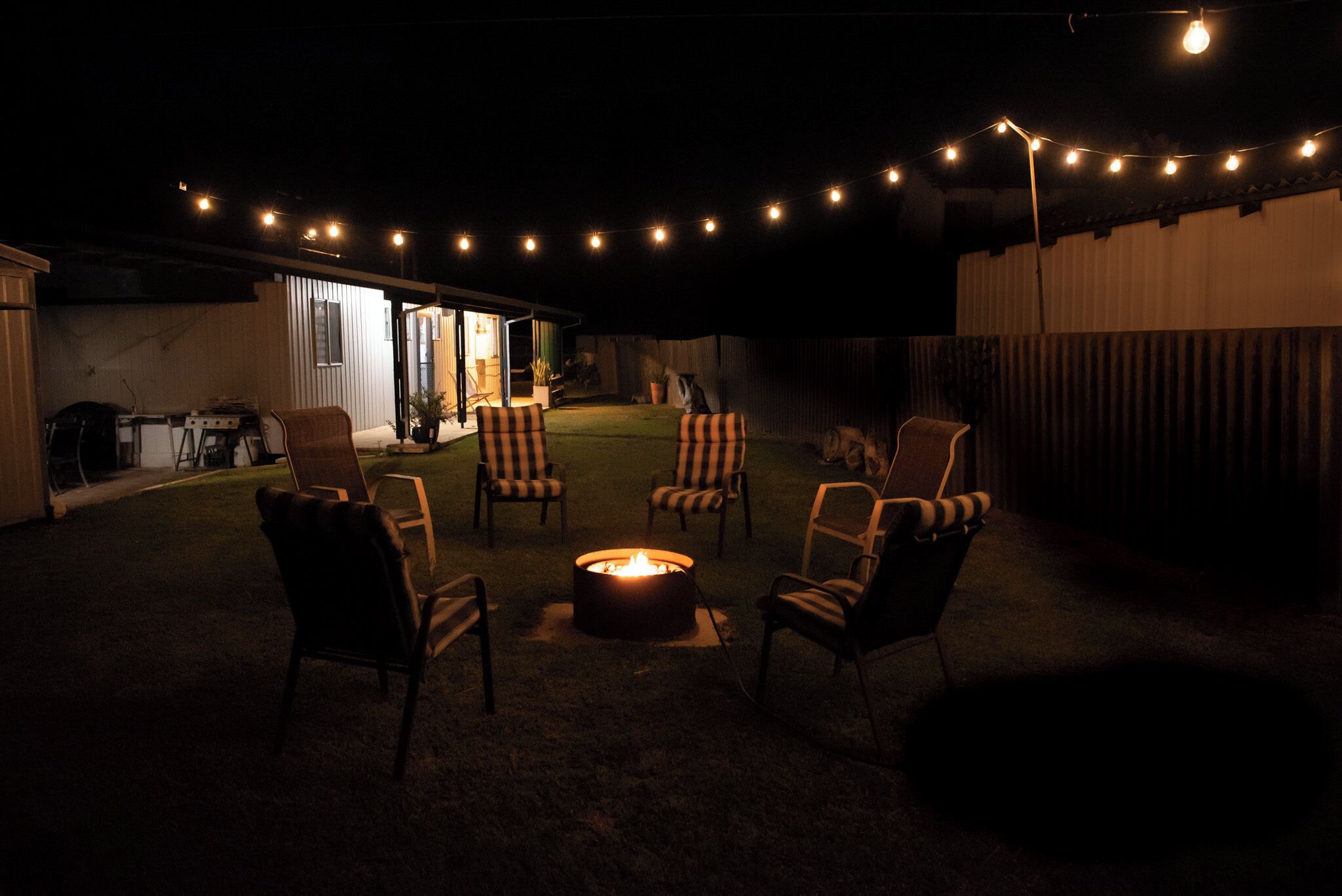 A backyard with a fire pit, chairs, and string lights.