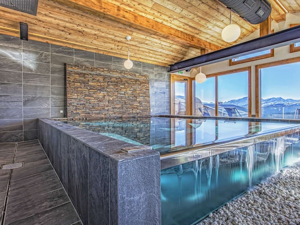 Un área de spa moderna con un jacuzzi de vidrio, paredes de piedra y techo de madera.